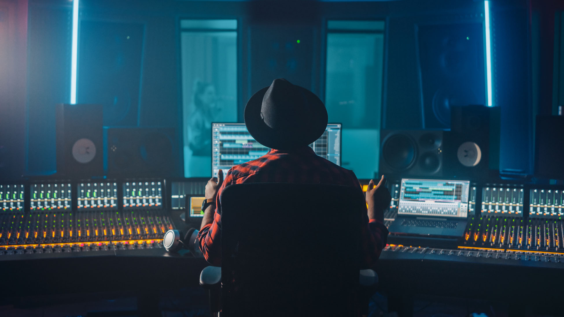 Producer, Audio Engineer Uses Control Desk for Recording New Album Track in Music Record Studio, in the Soundproof Room Musician, Artist, Performer Sings a Song from New Album. Back View